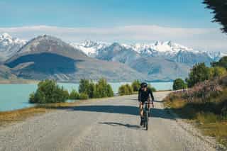 Un cycliste roule sur une route de gravier près d'un lac avec une vue sur les montagnes