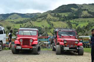 Foto van twee rode jeeps met als achtergrond een groene vallei tijdens een fietsreis met Veloglobe in Colombia.