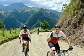 Veloglobe deelnemers aan het lachen en bergop aan het fietsen op een gravelparcour in Colombia.