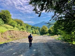 Een Veloglobe-fietser rijdt op een ruige bergweg, omringd door bomen met uitzicht op bergen in Georgië.