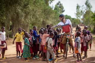 Vrolijke groep fietsers in Veloglobe-tenue lachend na avontuurlijke rit, met de weelderige, tropische omgeving van Rwanda op de achtergrond.