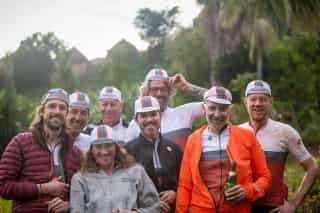 Vrolijke groep fietsers in Veloglobe-tenue lachend na avontuurlijke rit, met de weelderige, tropische omgeving van Rwanda op de achtergrond.