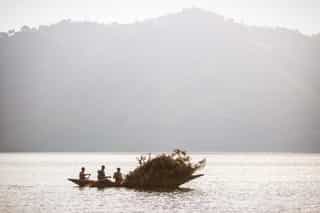 Petit bateau avec des locaux transportant des produits agricoles sur le lac Burera près de Cyuza, avec le paysage apaisant des collines rwandaises en arrière-plan.