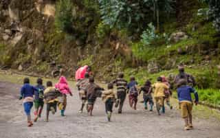 Enfants courant sur un chemin rural au Rwanda, entourés de nature luxuriante et de parois rocheuses, exprimant joie et liberté.