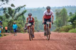 Twee Veloglobe deelnemers diep in de camera aan het kijken terwijl ze net de tip van een berg bereiken in Rwanda.